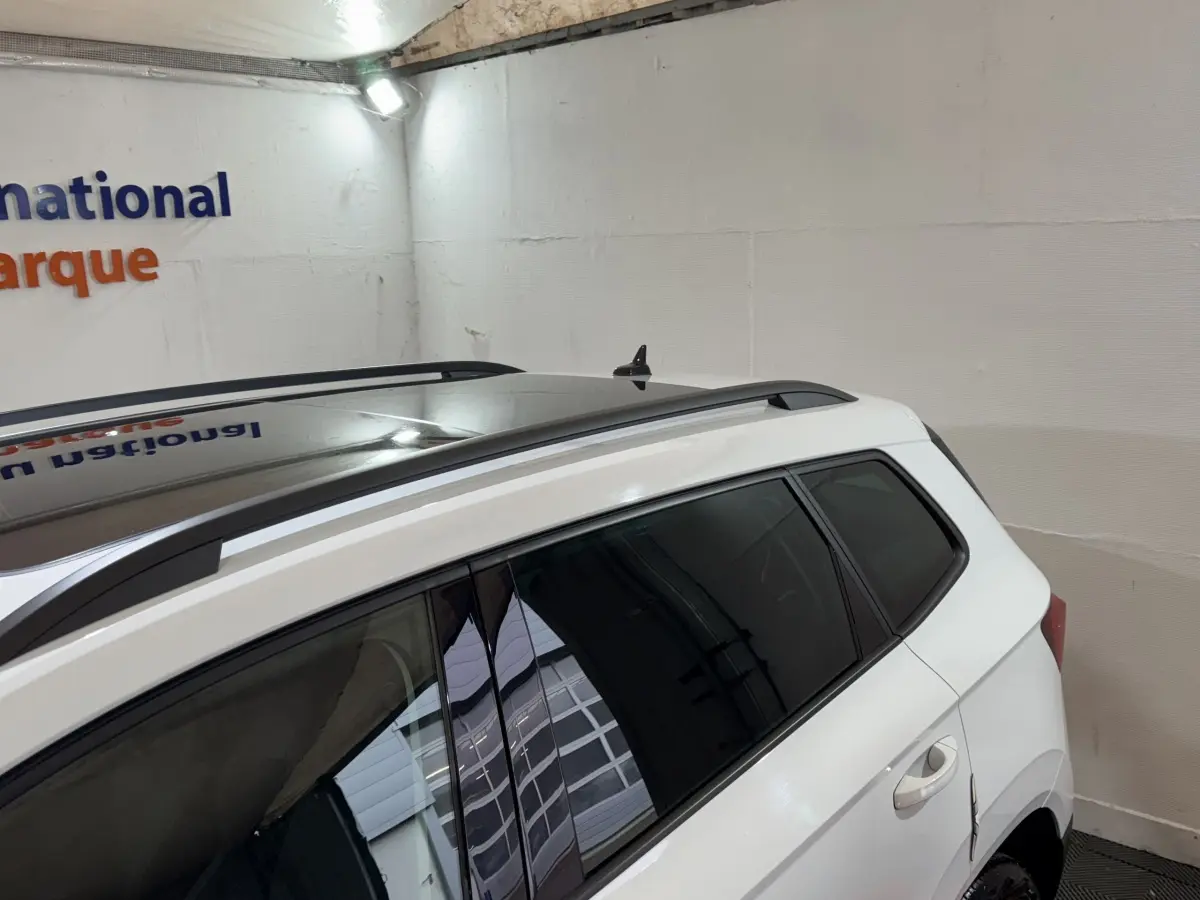 Vue côté droit arrière du SKODA KAROQ blanc avec toit panoramique et barres de toit noires visibles.