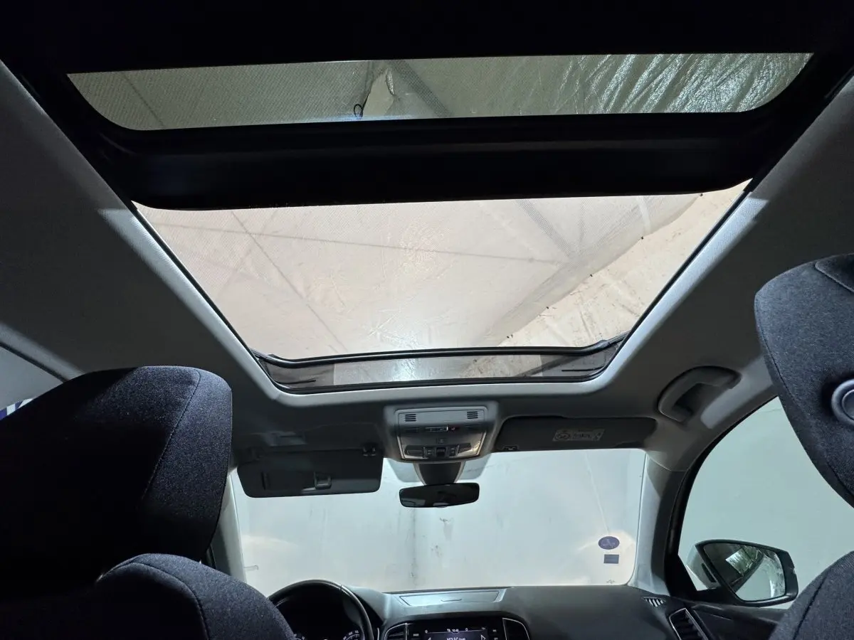 Vue intérieure avant du Skoda Karoq blanc 2021, mettant en valeur le toit panoramique et les sièges noirs.