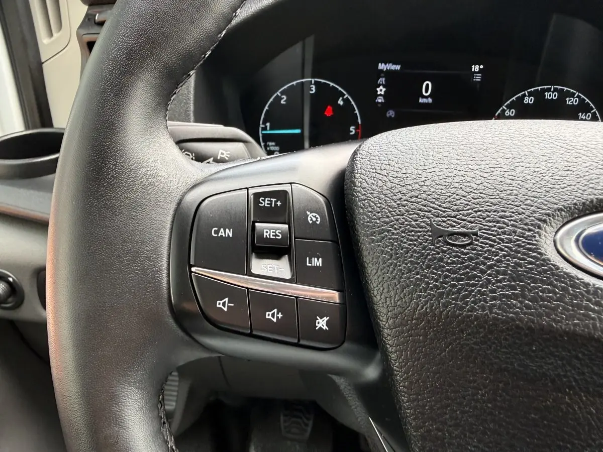 Gros plan sur le volant en cuir noir du Ford Transit Fourgon 2024 avec commandes intégrées et tableau de bord numérique.