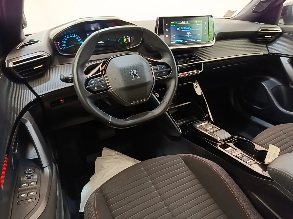 Vue intérieure avant droite du Peugeot E-2008 électrique gris clair, volant cuir et écran tactile central lumineux.