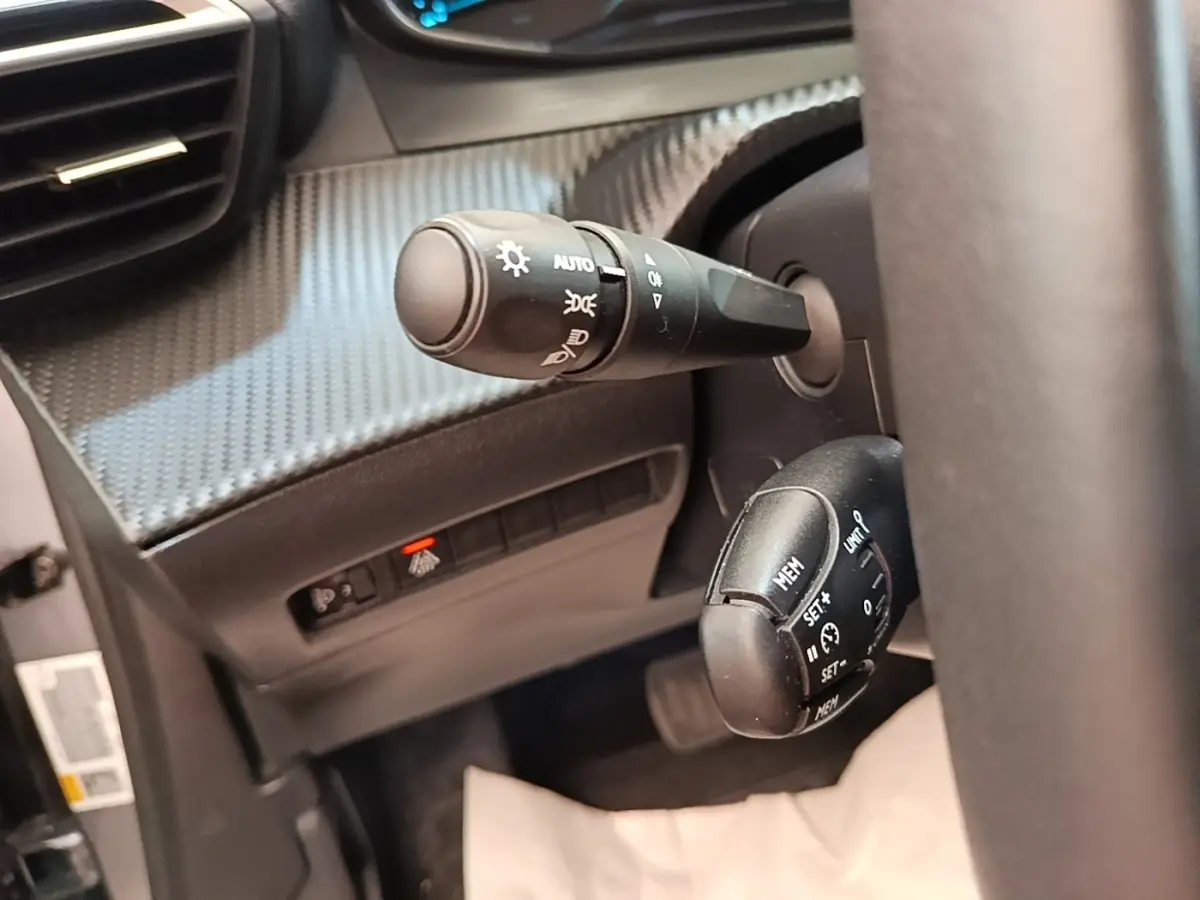 Gros plan sur les commandes au volant du Peugeot E-2008 électrique gris clair, avec réglages feux et régulateur de vitesse.