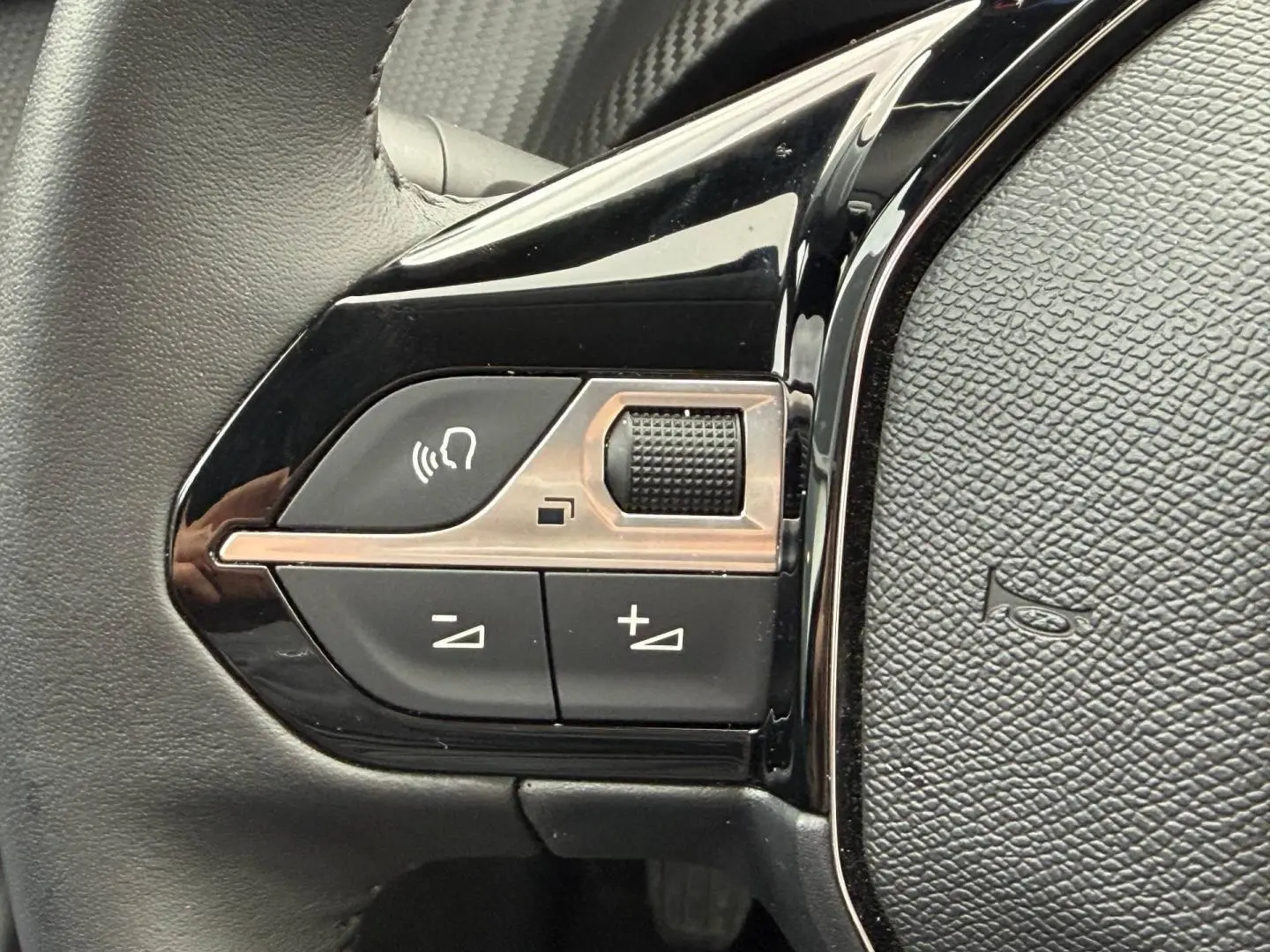 Gros plan sur les commandes audio et vocales noires sur le côté gauche du volant de la Peugeot 208 noir Perla Nera.