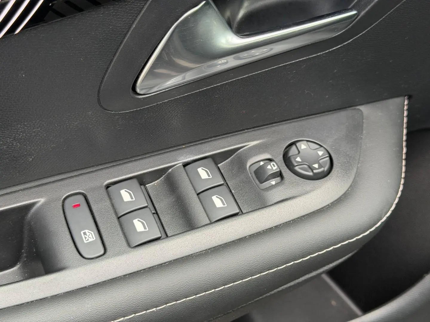 Gros plan sur la commande des vitres et rétroviseurs côté conducteur de la Peugeot 208 noir Perla Nera avec surpiqûres blanches.