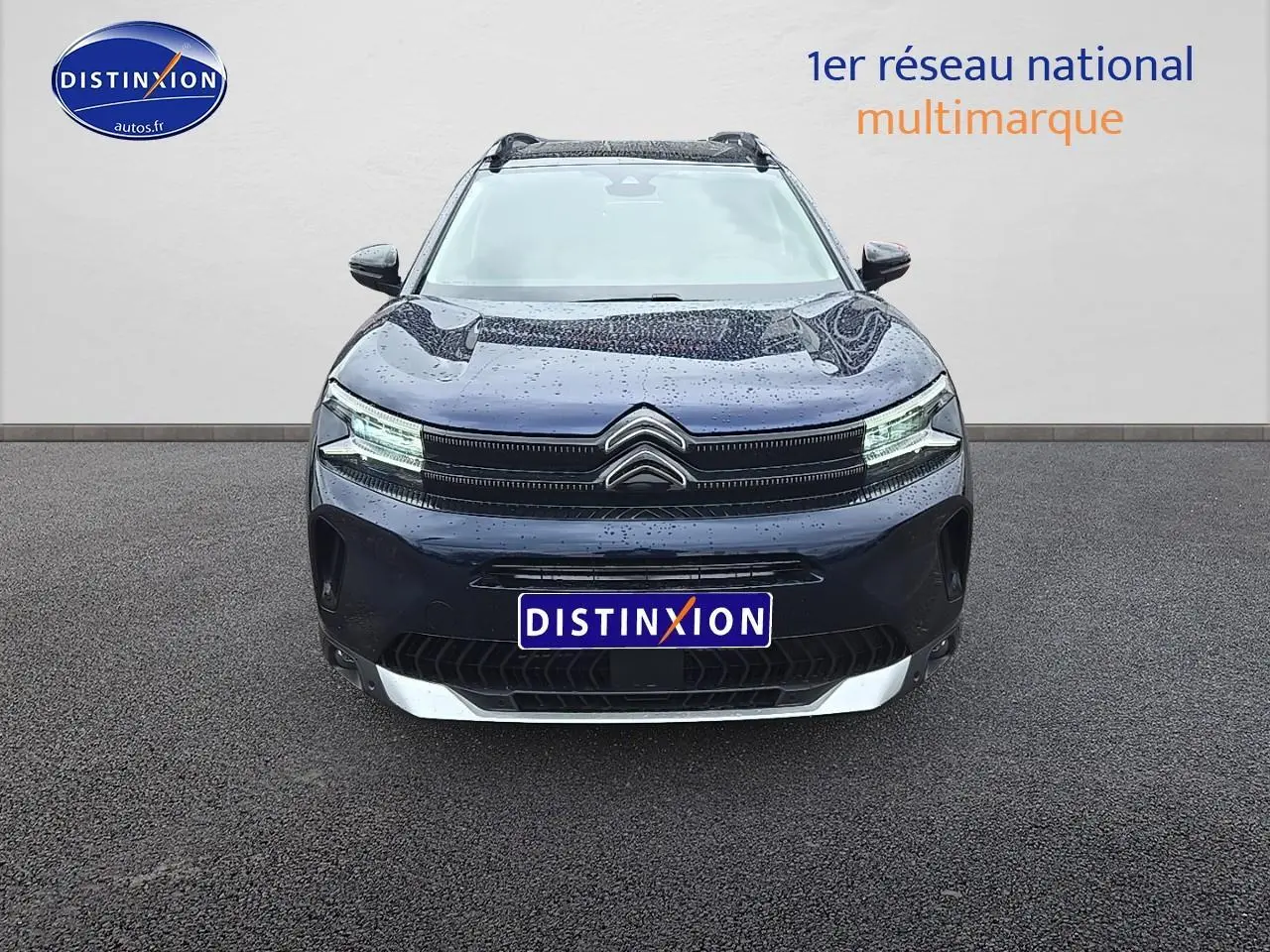 Vue frontale d'un Citroën C5 Aircross bleu eclipse avec phares LED allumés sur sol goudronné.