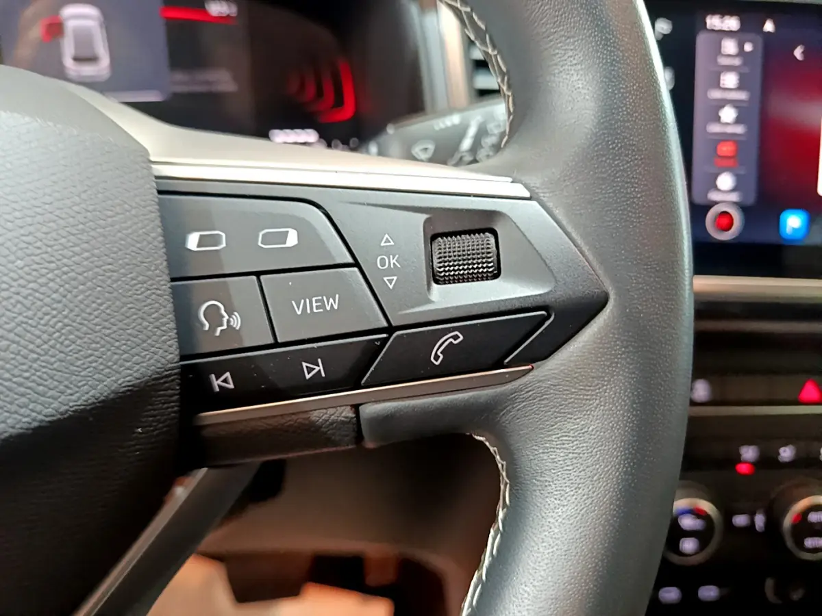 Gros plan sur les commandes du volant cuir noir du SEAT Ateca 2022, avec écran tactile et tableau de bord en arrière-plan.