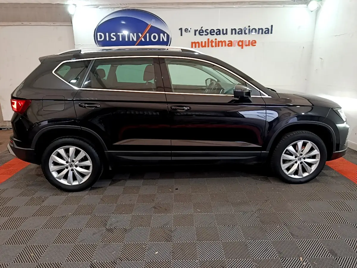 Profil côté gauche d'un SUV SEAT Ateca noir 2022 avec jantes alliage et barres de toit chromées dans un showroom.