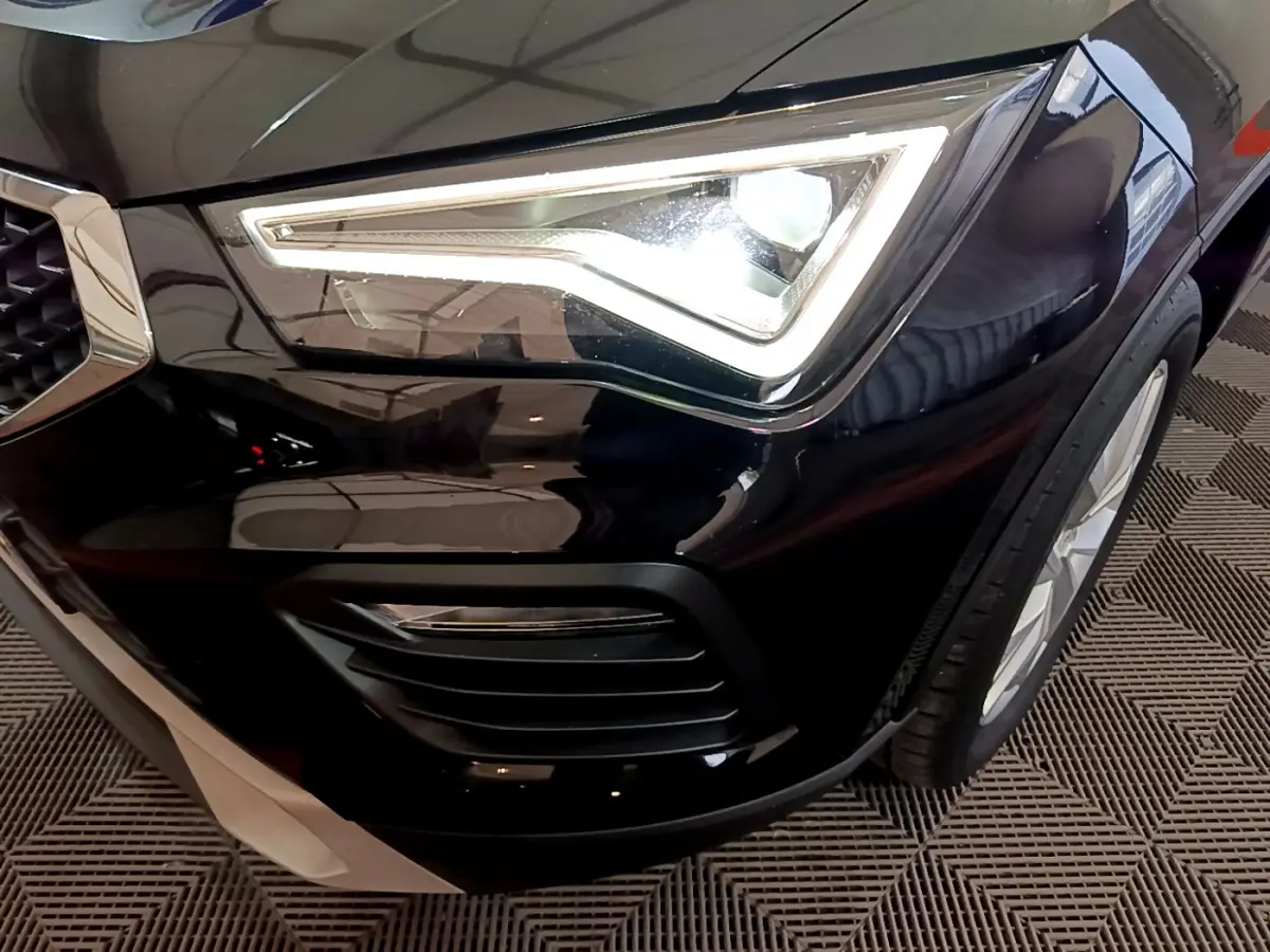 Gros plan sur le phare avant droit allumé du SEAT Ateca noir, mettant en valeur la calandre et la roue avant.