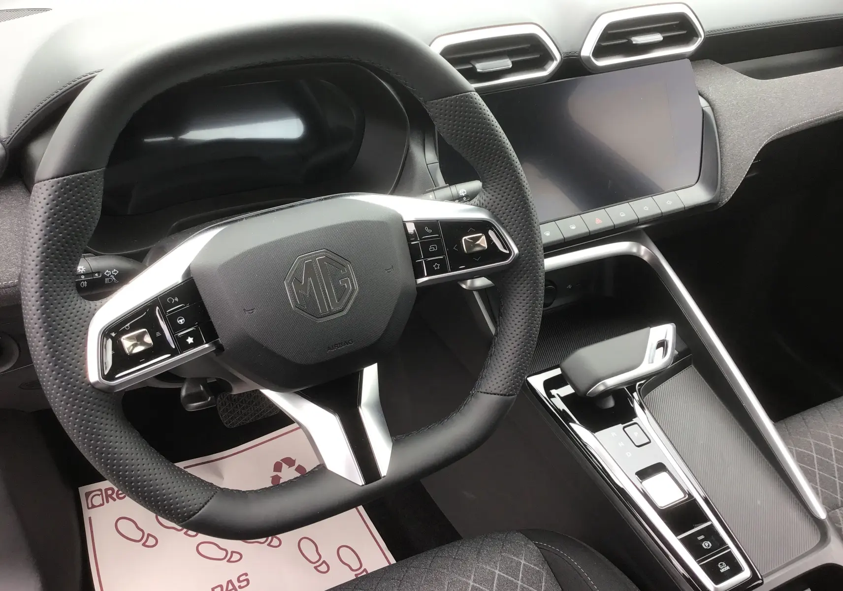 Vue intérieure centrée sur le volant noir perforé et la console centrale avec écran tactile du MG ZS 1.5 L Hybrid+ Cosmic Silver.