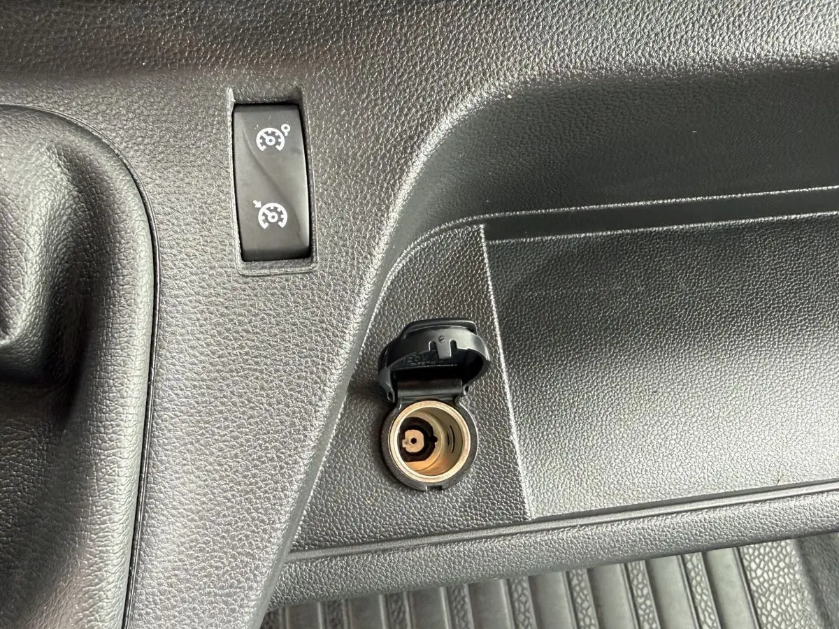 Gros plan sur la prise 12V ouverte et le bouton de régulateur de vitesse sur le tableau de bord noir du Renault Master blanc.