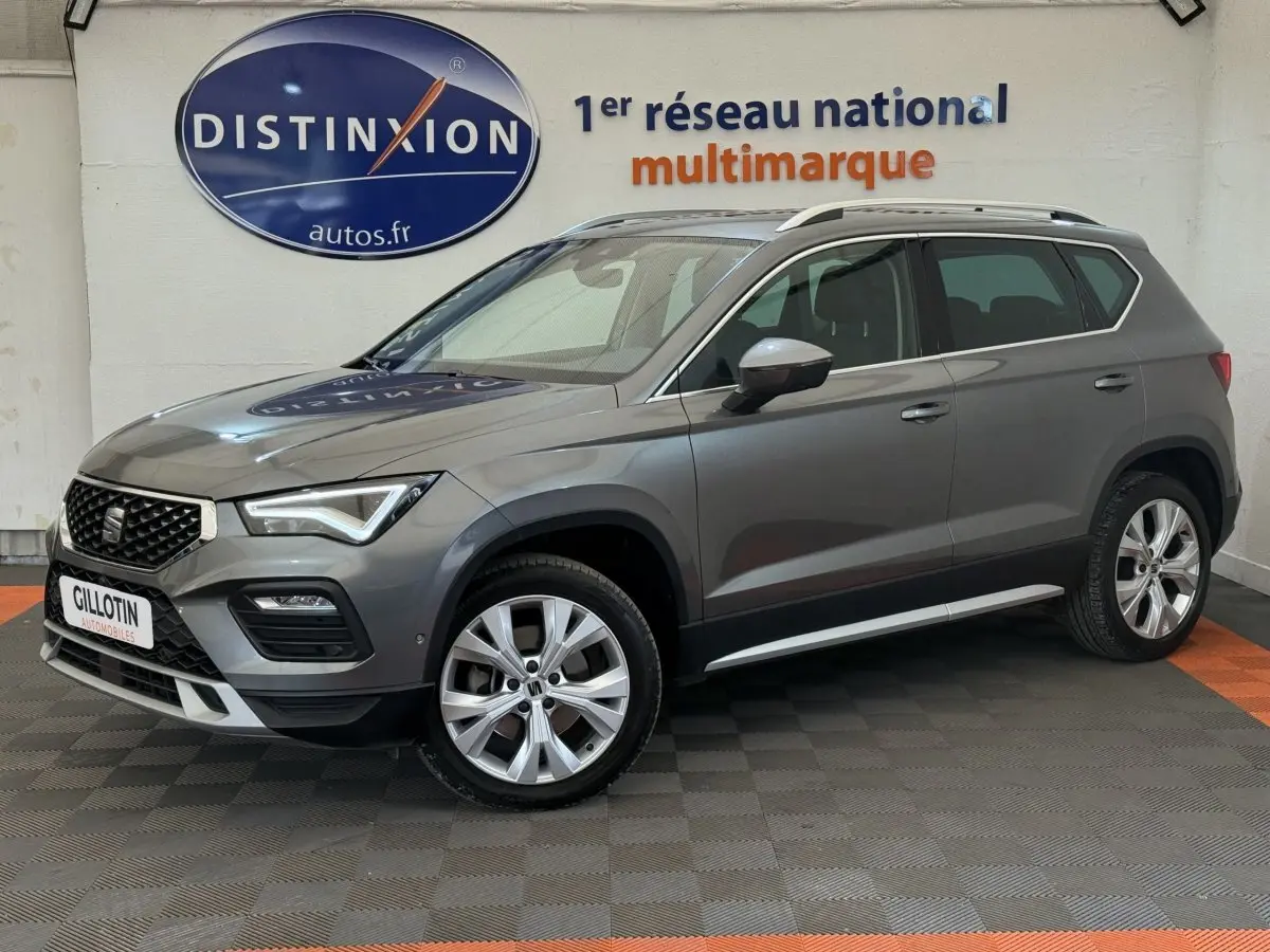 Vue 3/4 avant droit d'un SUV SEAT Ateca gris clair 2023 avec jantes alliage et barres de toit chromées.