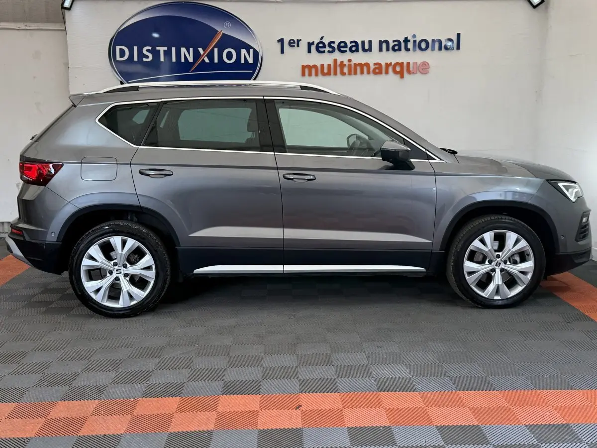 Vue de profil côté gauche d'un SEAT Ateca gris clair 2023 avec jantes alliage et barres de toit chromées.