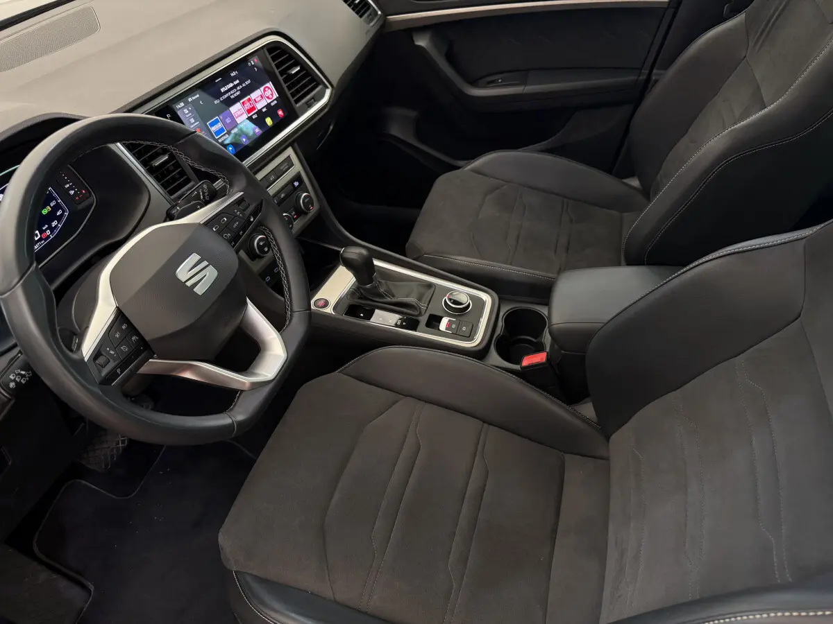 Intérieur du SEAT Ateca 2023 vu côté conducteur, sièges noirs, volant multifonctions et écran tactile central visible.