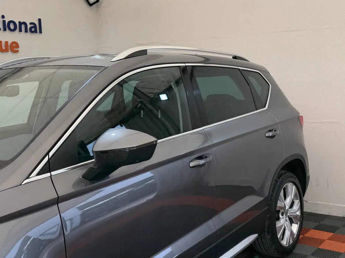 Vue côté gauche du SEAT Ateca gris clair 2023, mettant en valeur les jantes et les barres de toit chromées.