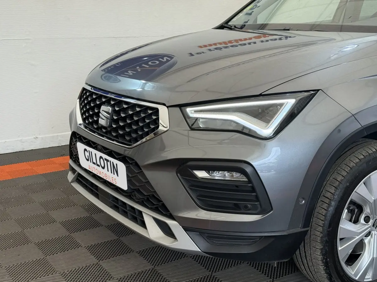 Vue 3/4 avant droit d'un SEAT Ateca gris clair avec calandre noire à motif losange et phares LED distinctifs.