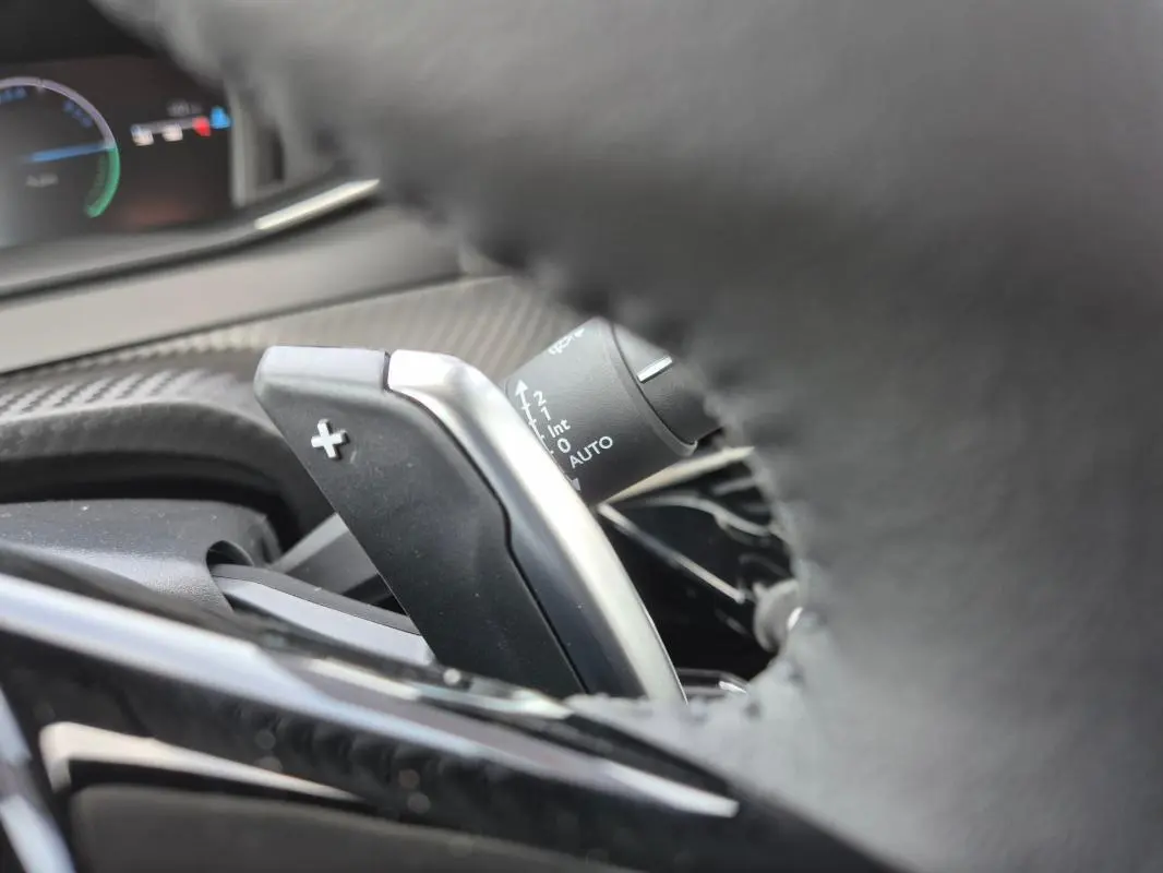 Gros plan sur la palette de changement de vitesse "+" derrière le volant du Peugeot 208 blanc, intérieur moderne.