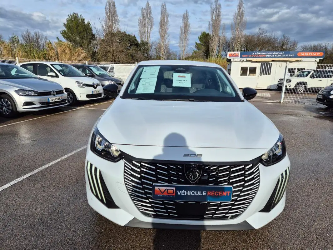 Vue avant d'une Peugeot 208 Hybrid 110 e-DCS6 Allure blanche avec calandre noire et feux LED diurnes verticaux.
