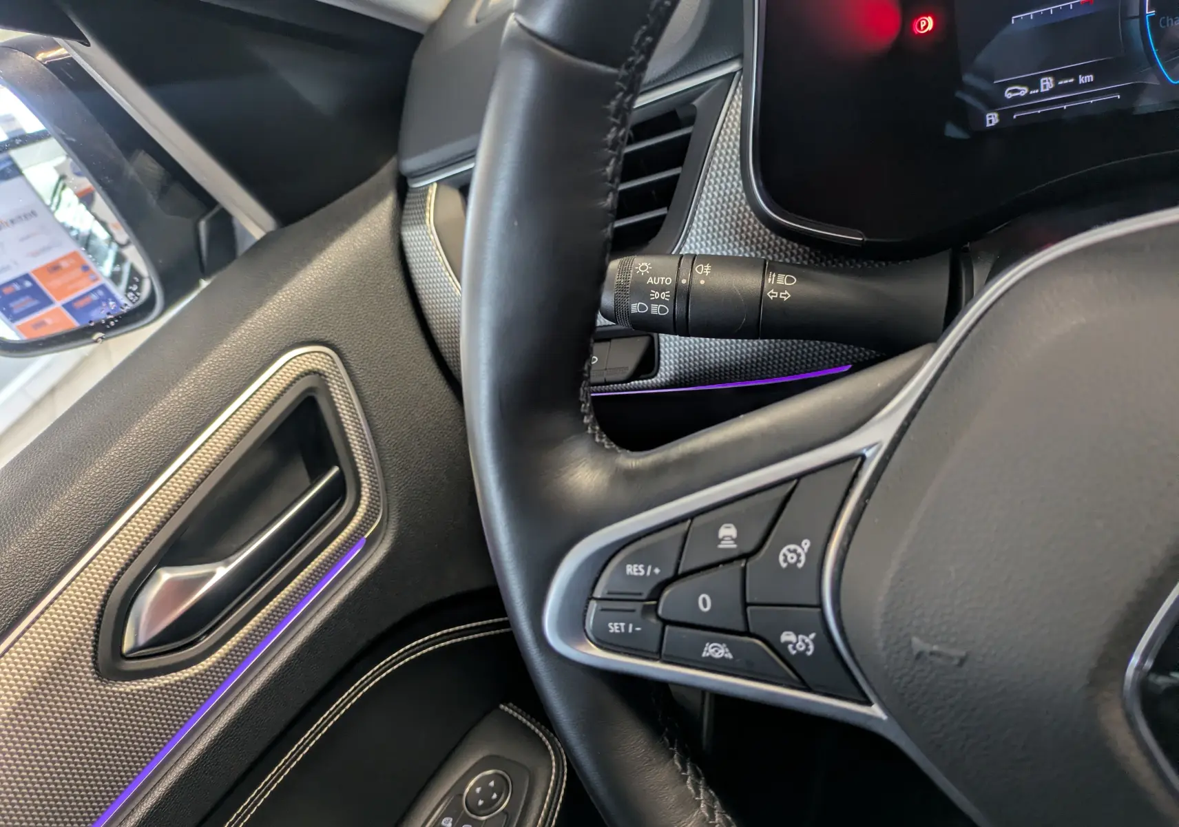 Vue rapprochée de l’intérieur côté gauche du Renault Arkana noir métal, montrant le volant avec commandes et la portière avec éclairage d’ambiance violet.