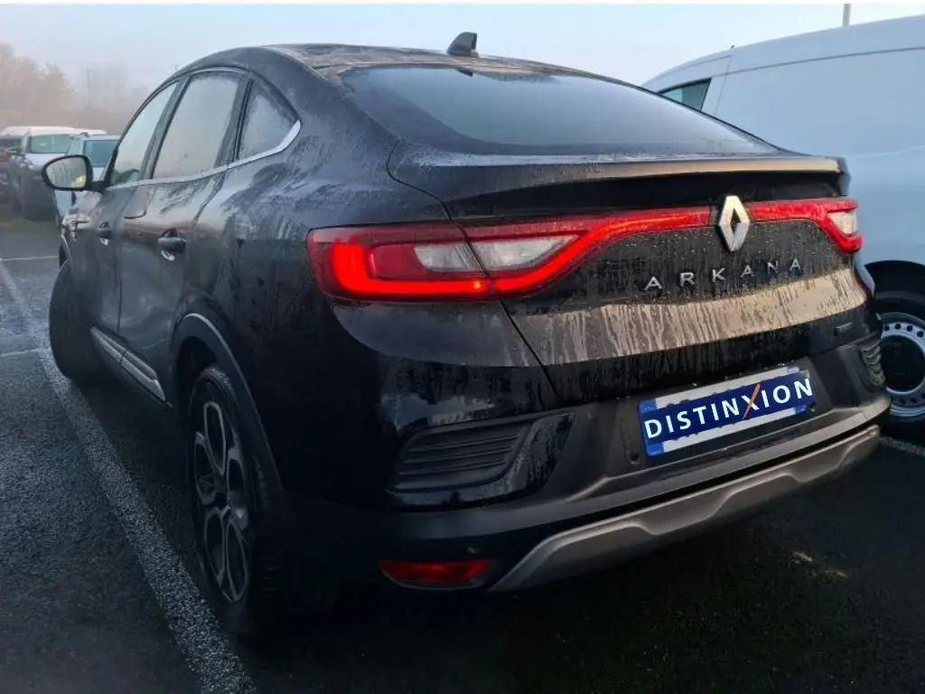 Profil côté gauche d'une Renault Arkana noire métal 2023, avec jantes bi-ton et toit incliné dans un showroom.