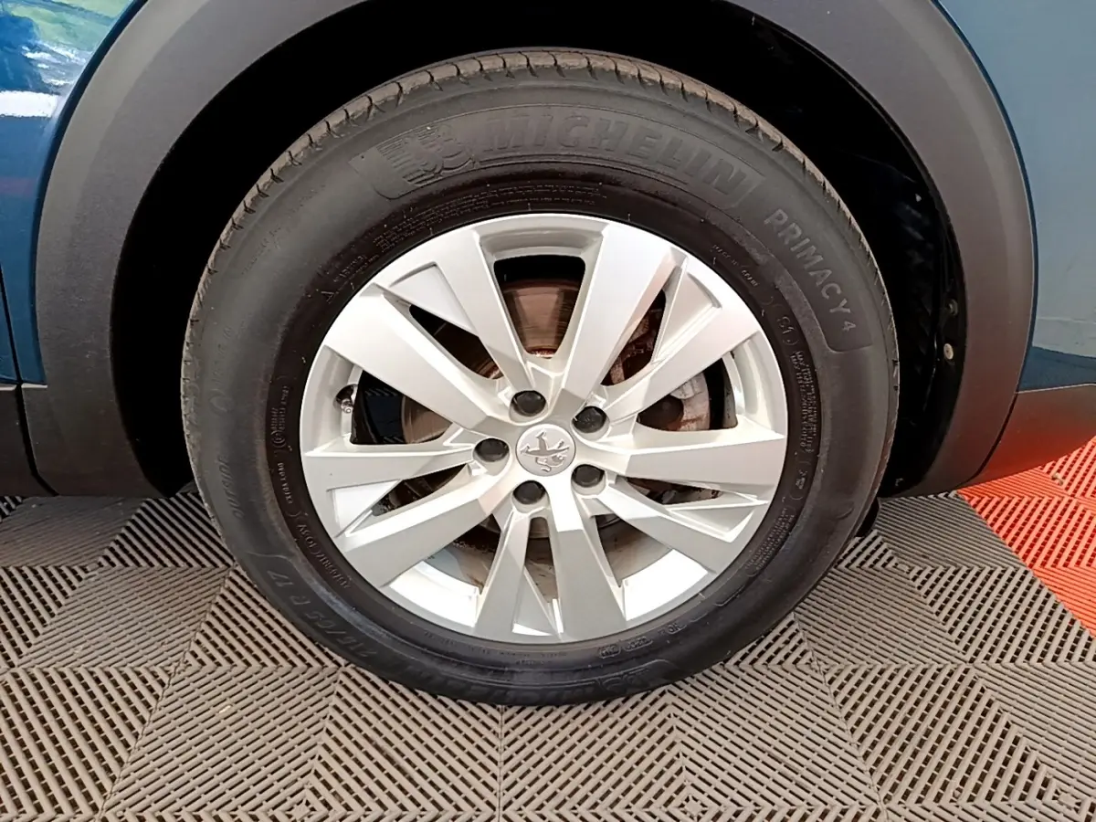 Gros plan sur la roue avant gauche d’un Peugeot 5008 bleu avec jante alliage argentée et pneu Michelin.