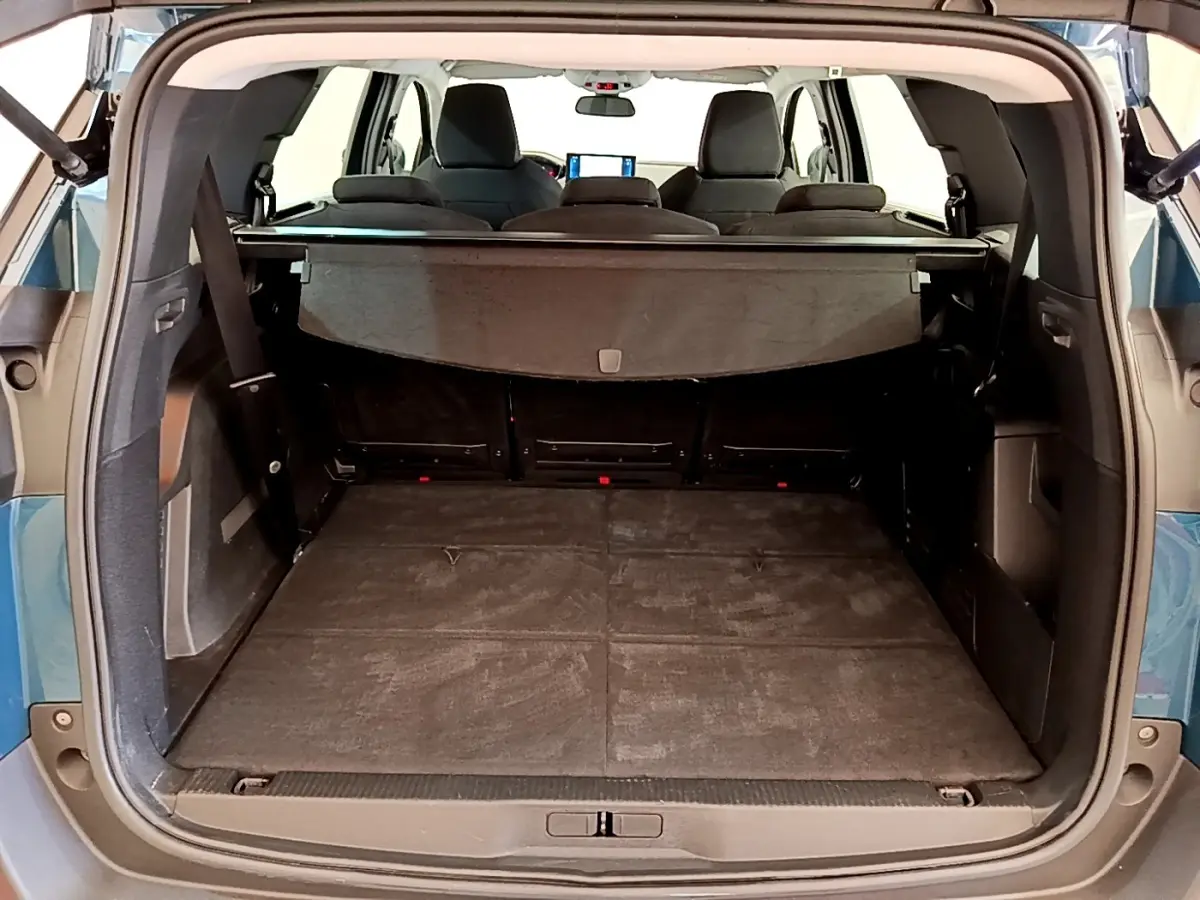 Vue arrière du coffre ouvert du Peugeot 5008 bleu, montrant la tablette cache-bagages et les sièges rabattus.