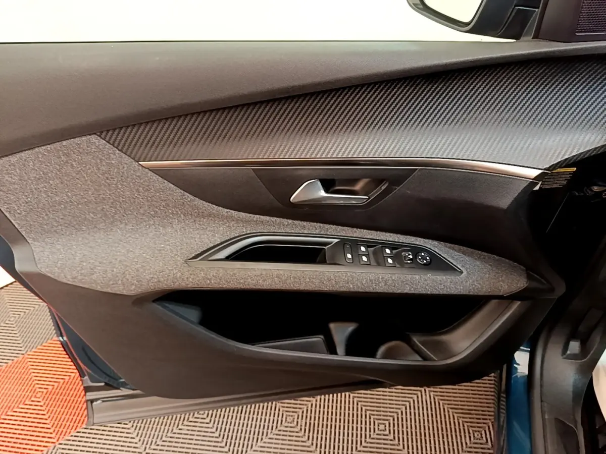 Vue intérieure côté gauche de la porte avant d’un Peugeot 5008 bleu, avec commandes de vitres et poignée argentée.