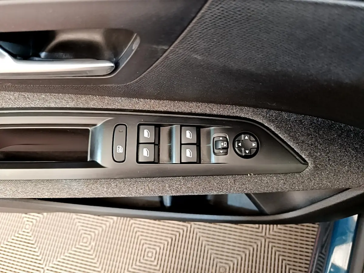 Commande des vitres et rétroviseurs sur la porte côté conducteur d’un Peugeot 5008 bleu, finition tissu gris.