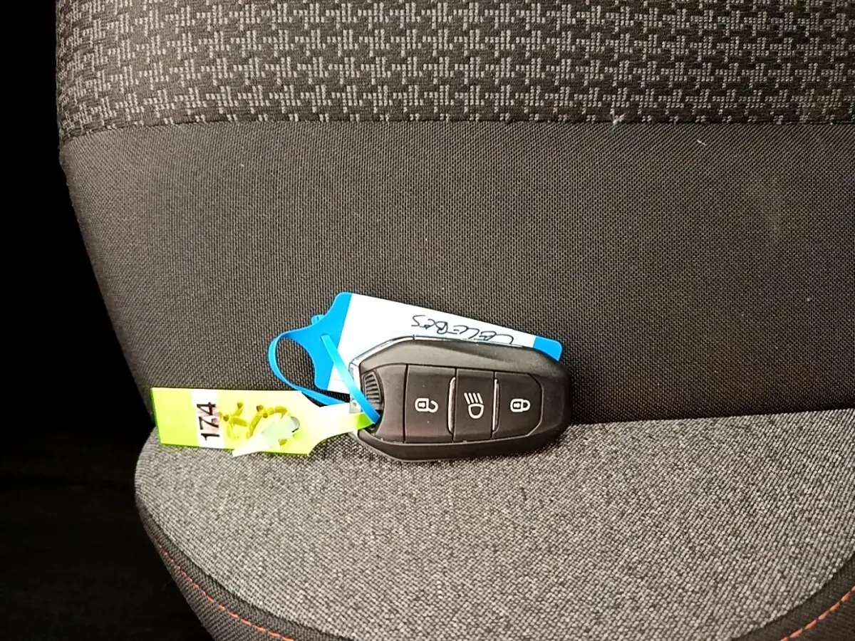 Gros plan sur la clé noire du Peugeot 5008 posée sur un siège tissu gris foncé à coutures rouges.