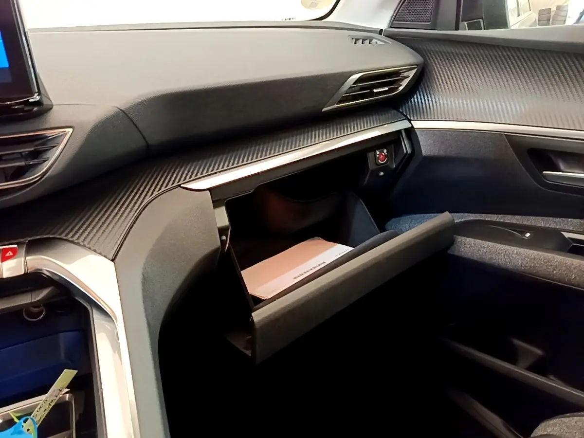 Intérieur du Peugeot 5008 2021, vue côté passager sur la boîte à gants ouverte et tableau de bord noir texturé.