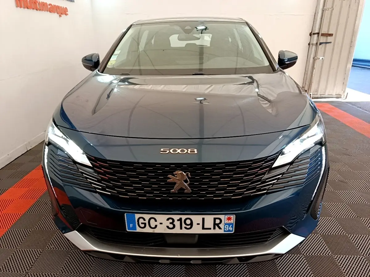 Vue frontale d’un Peugeot 5008 bleu avec calandre noire et phares LED allumés en intérieur.