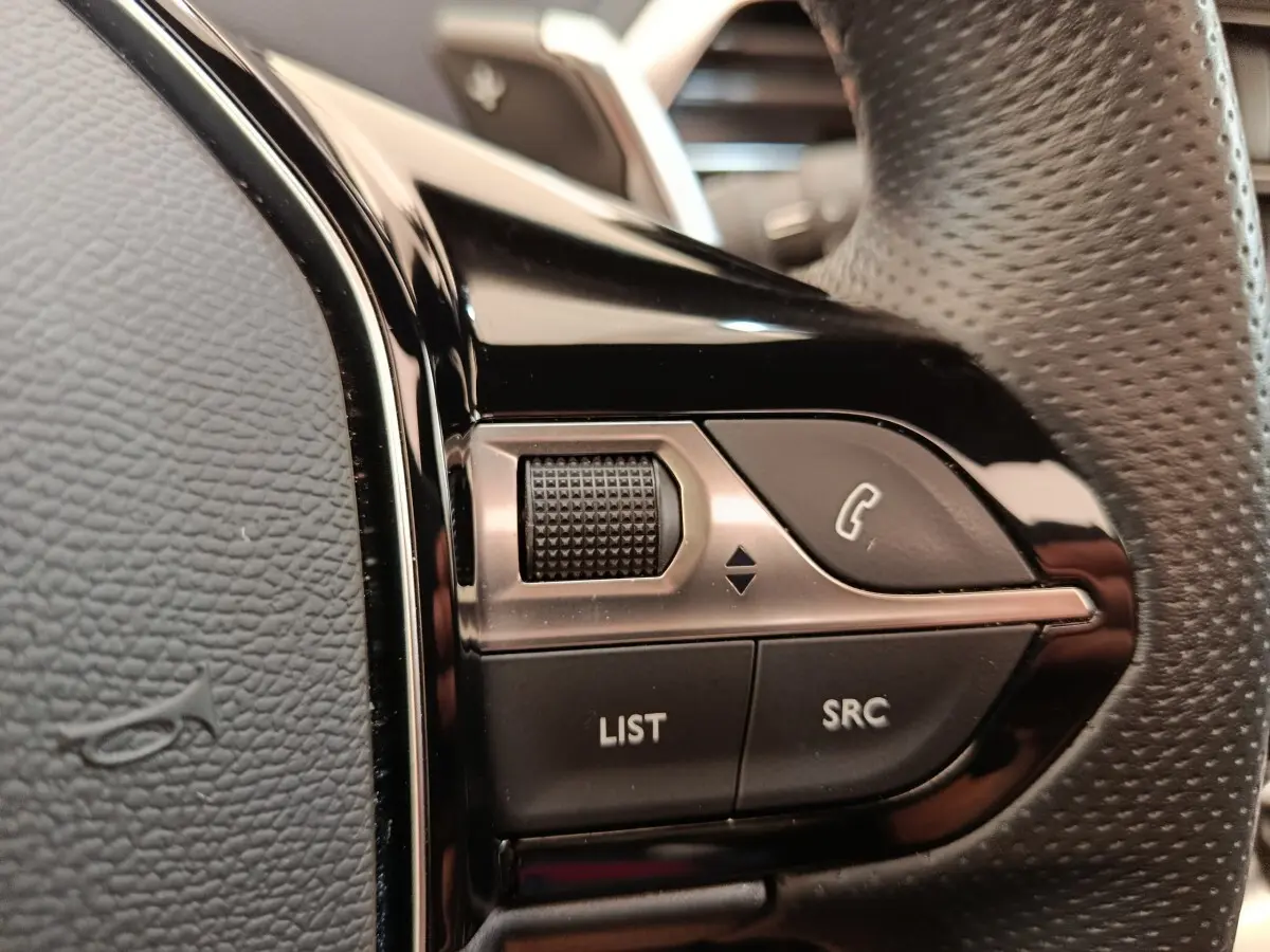 Gros plan sur les commandes noires du volant perforé du Peugeot 3008 GT Pack 2022, côté gauche.