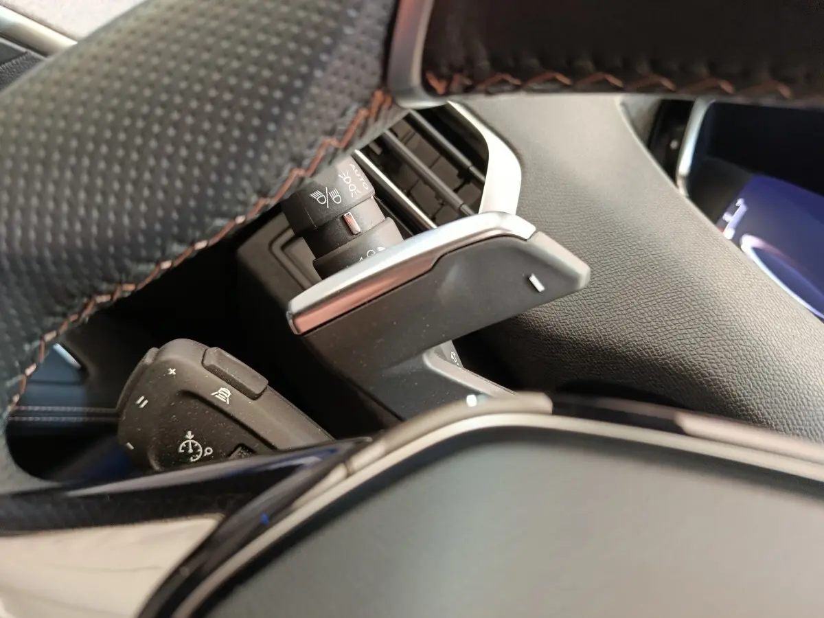 Gros plan sur palettes de changement de vitesse derrière le volant cuir noir du Peugeot 3008 rouge, version GT Pack.