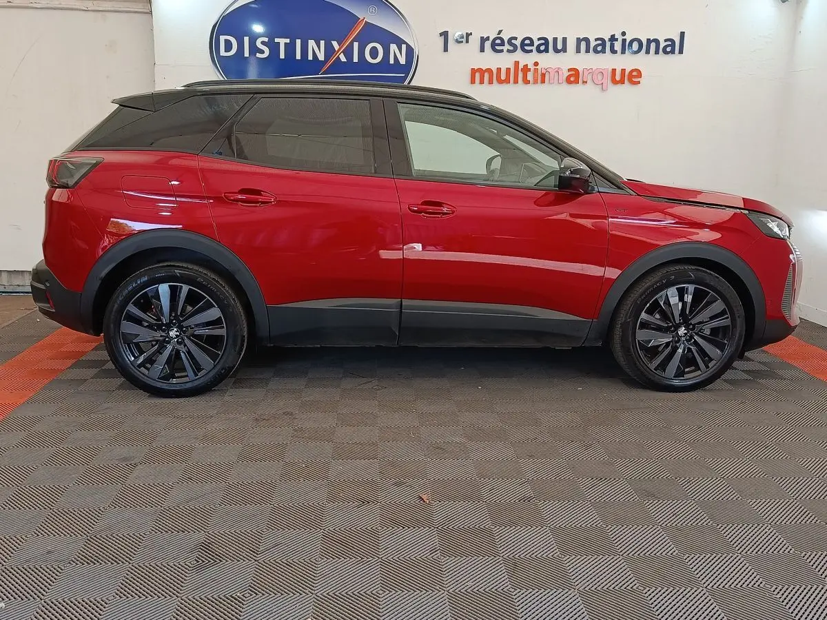 Vue latérale droite d'un Peugeot 3008 rouge 2022 avec jantes noires et toit noir, en intérieur showroom.