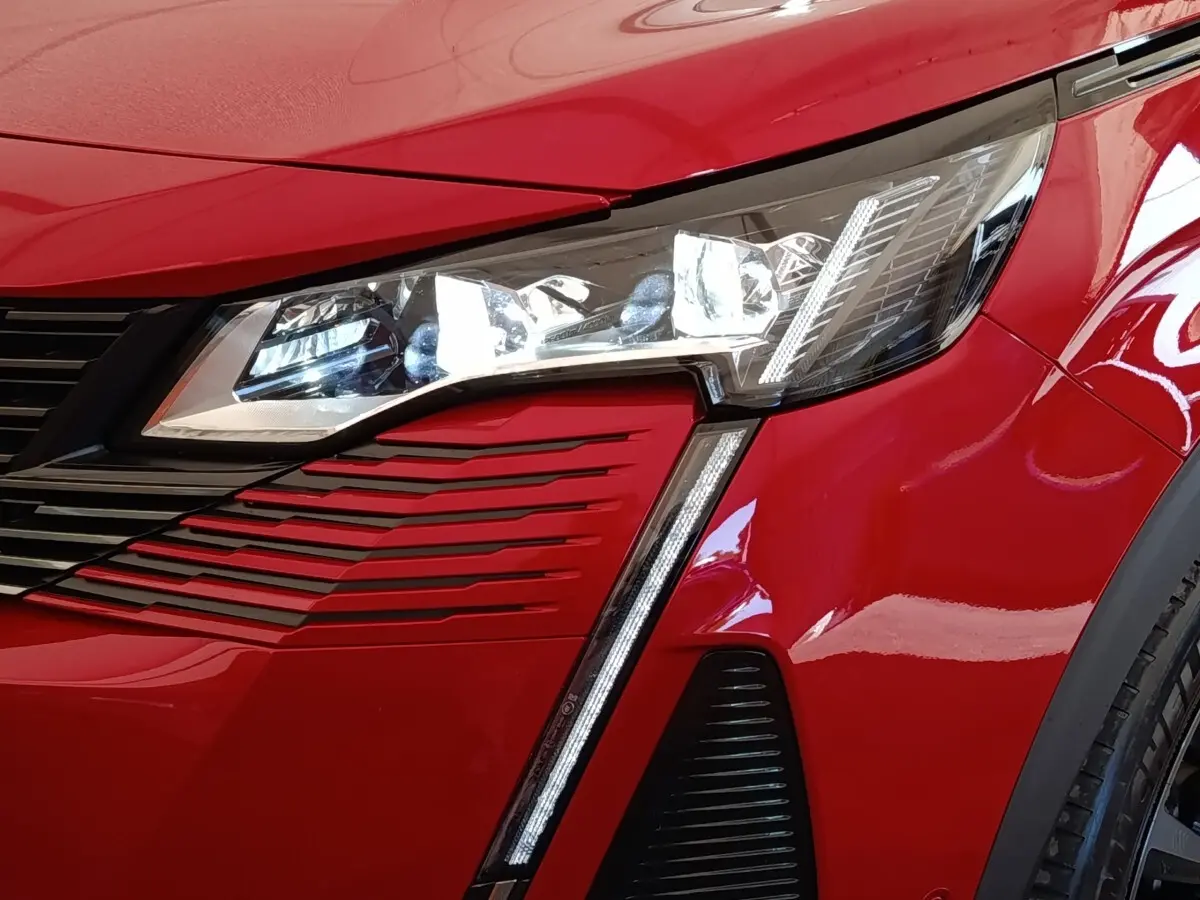 Gros plan sur l'avant droit rouge du Peugeot 3008 2022, mettant en valeur le phare LED et la calandre distinctive.