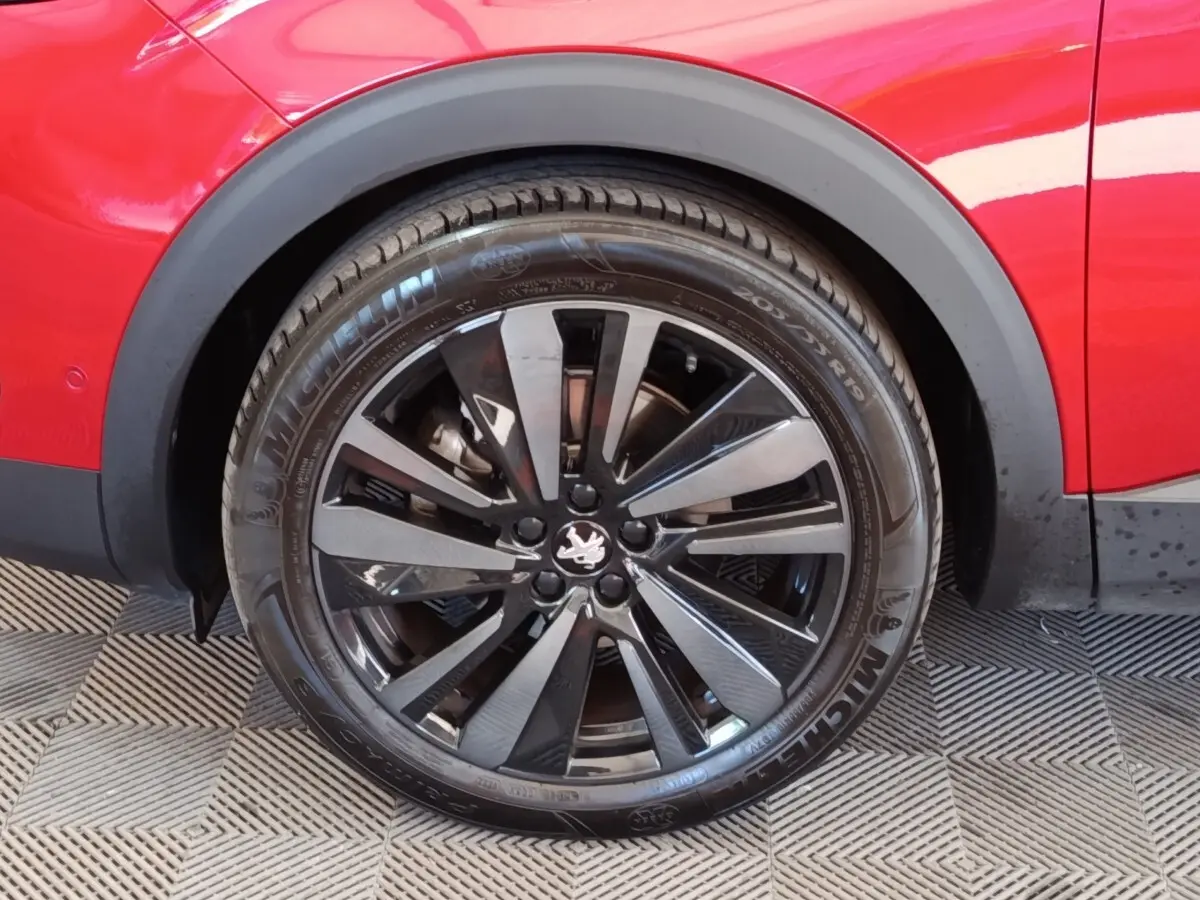 Gros plan sur la roue arrière droite d’un Peugeot 3008 rouge avec jante alliage noire brillante et logo lion central.