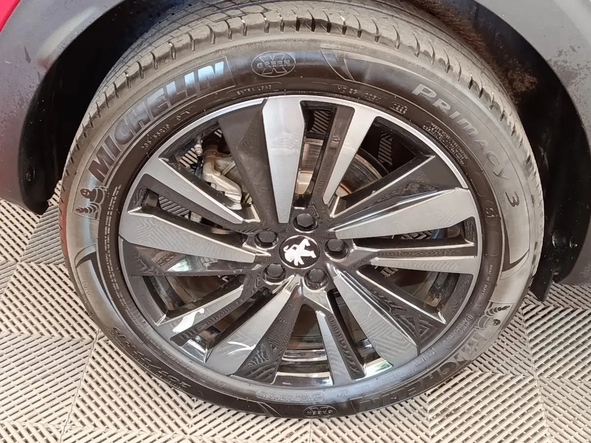 Gros plan sur la jante alliage noire et argentée du PEUGEOT 3008 rouge, avec logo lion au centre.