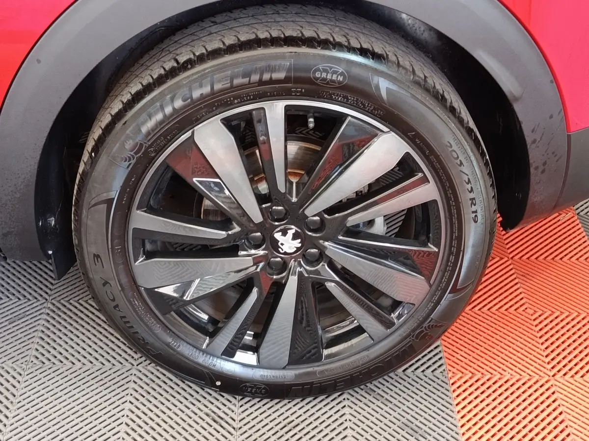 Gros plan sur la roue avant droite d’un Peugeot 3008 rouge avec jante alliage noire et logo lion au centre.