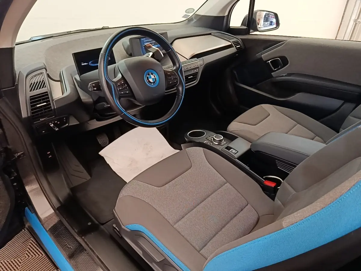 Vue intérieure côté conducteur de la BMW i3 120 Ah Atelier 2020, sièges gris avec surpiqûres bleues et volant cuir noir.