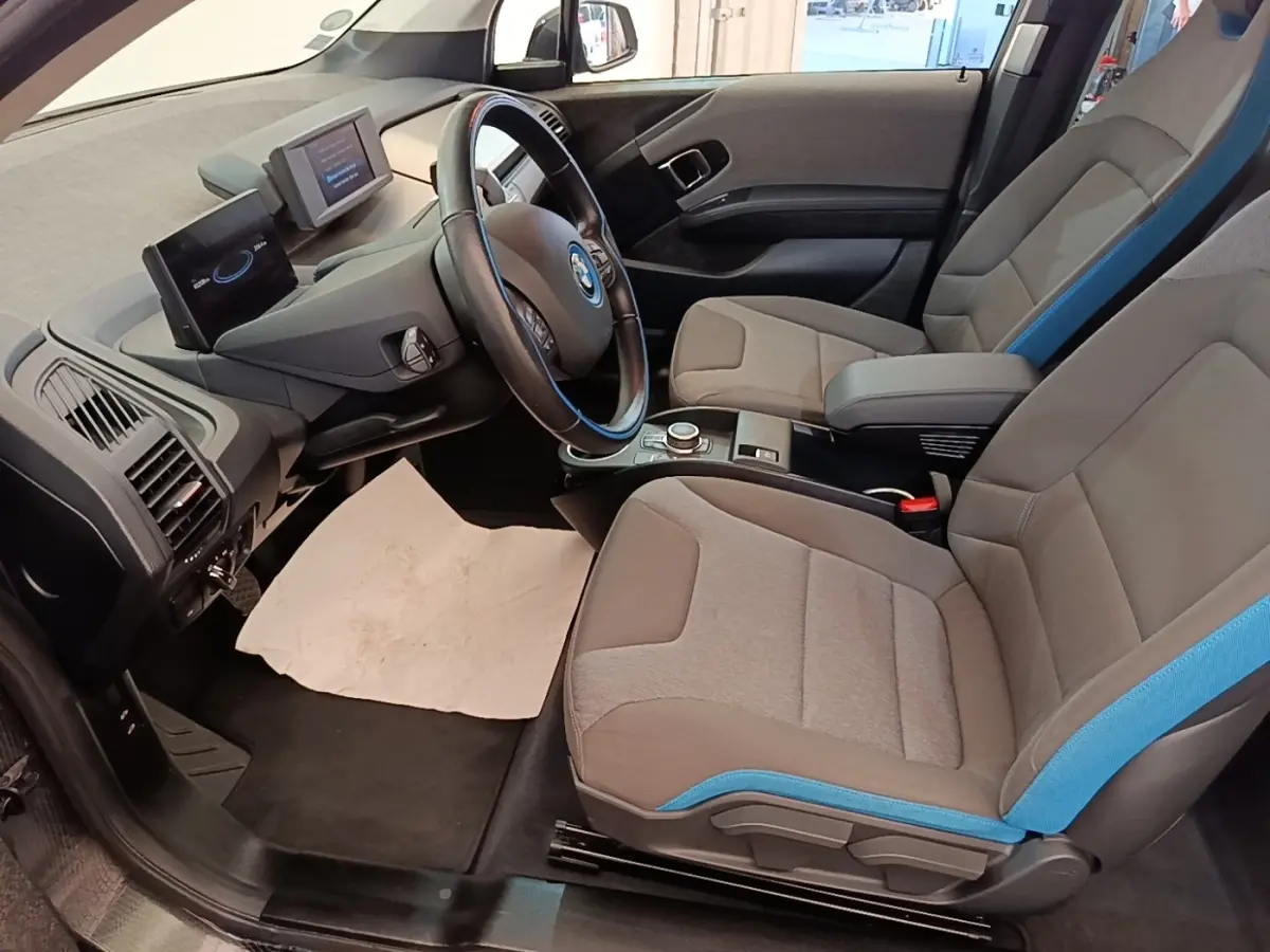 Vue intérieure côté conducteur de la BMW i3 120 Ah avec sièges gris et bleu et tableau de bord moderne.