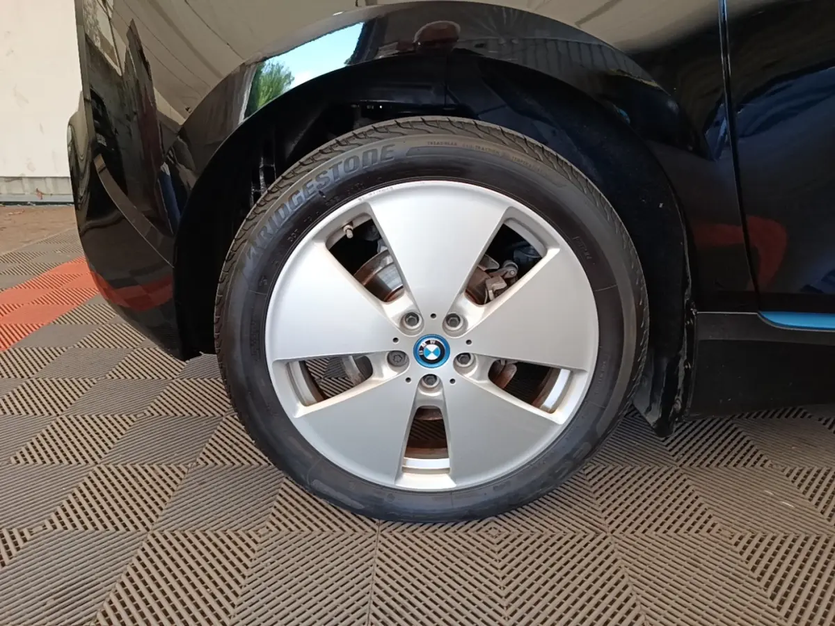 Gros plan sur la roue avant gauche argentée d’une BMW i3 noire, mettant en valeur la jante et le logo central.