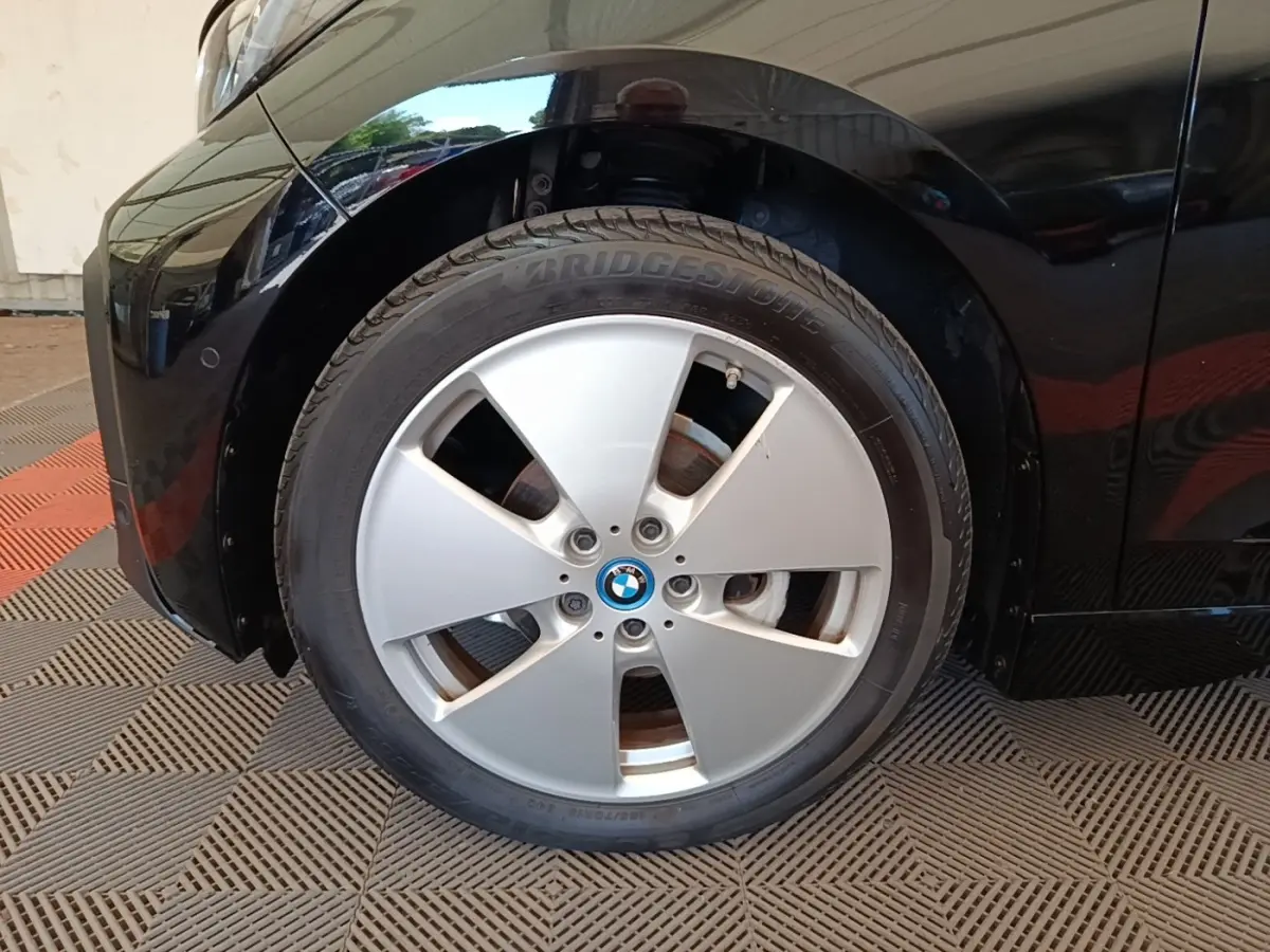 Gros plan sur la roue avant gauche d’une BMW i3 120 Ah noire, mettant en valeur la jante argentée et le logo BMW central.