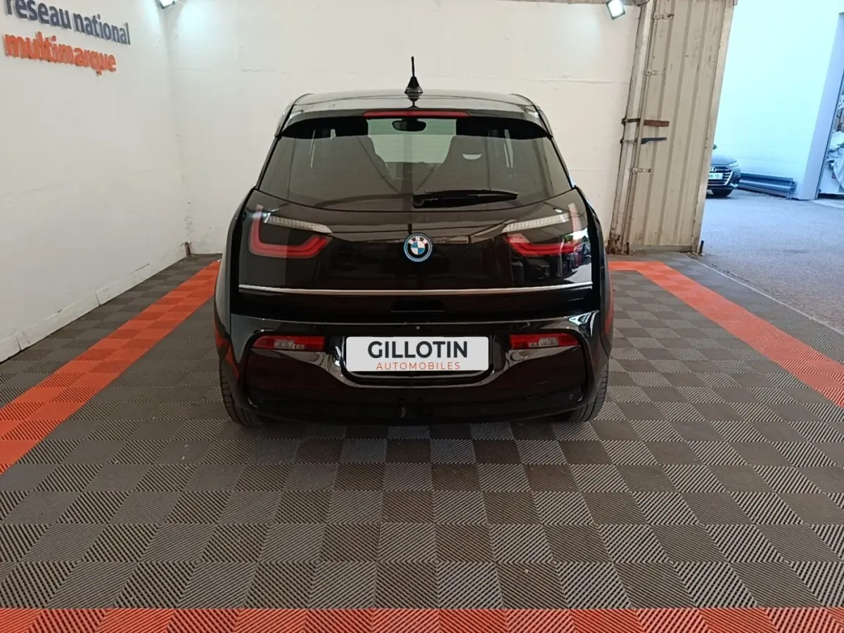 Vue arrière d'une BMW i3 120 Ah noire, stationnée en intérieur sur un sol à damiers gris et bandes orange.