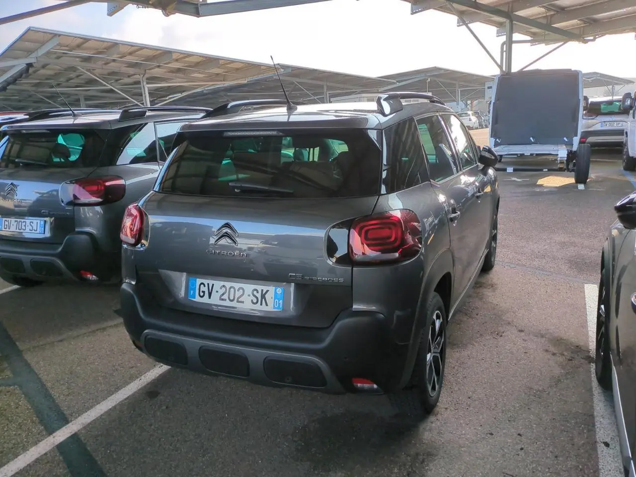 Vue 3/4 arrière droite d'un Citroën C3 Aircross gris foncé avec jantes alliage et barres de toit noires.