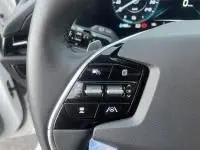 Gros plan sur les commandes au volant du Kia Niro EV blanc 2024, version Active 204 CV, avec tableau de bord numérique en arrière-plan.