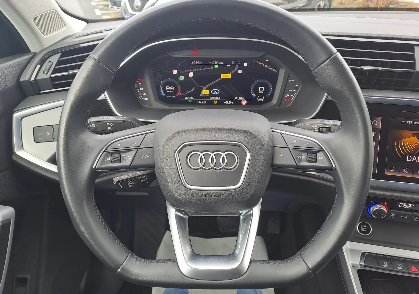 Vue intérieure centrée sur le volant cuir noir d’un Audi Q3 2023 avec tableau de bord numérique et écran tactile.