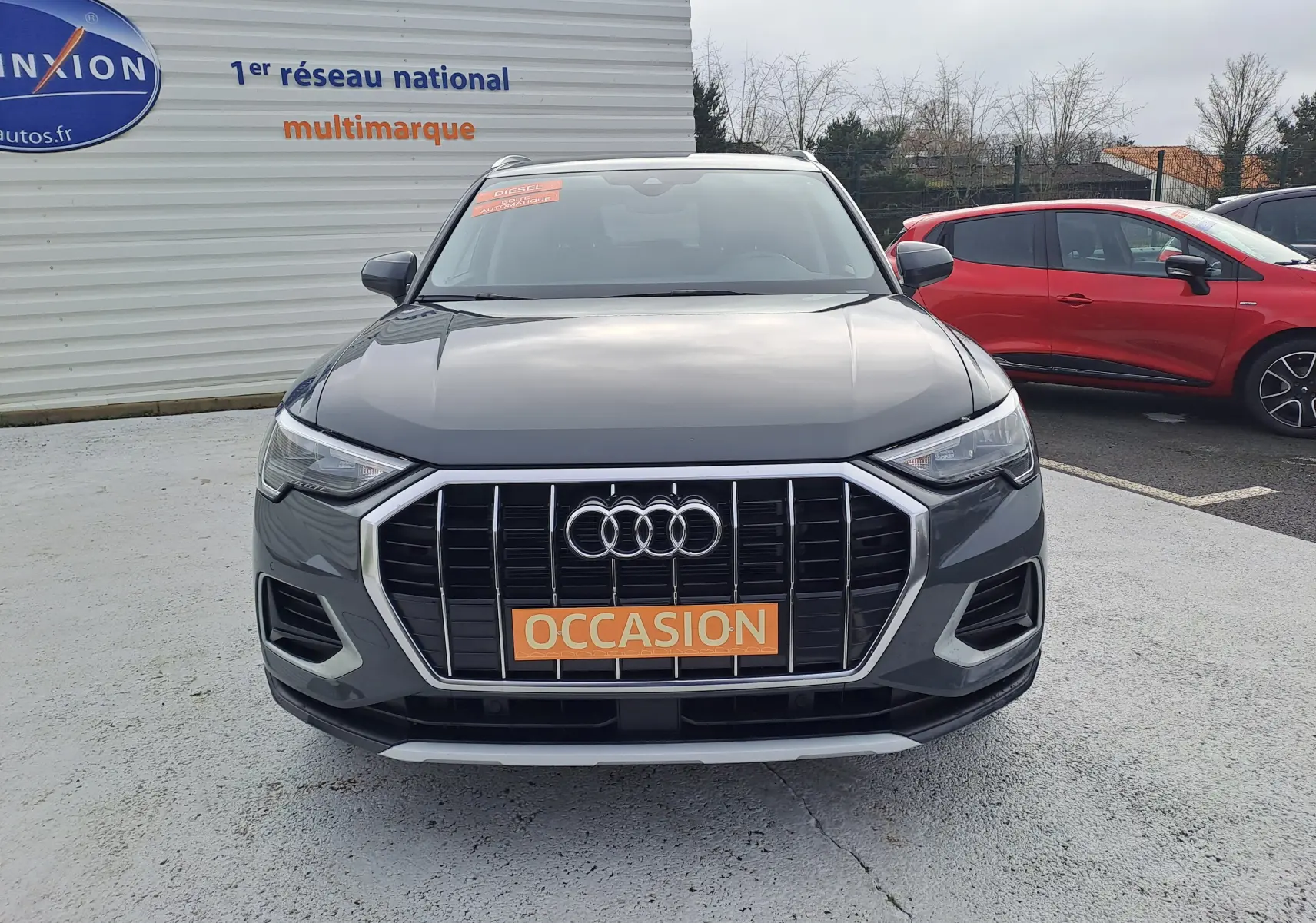 Vue frontale d'un Audi Q3 gris nano 2023 avec calandre large et plaque "OCCASION" orange visible.