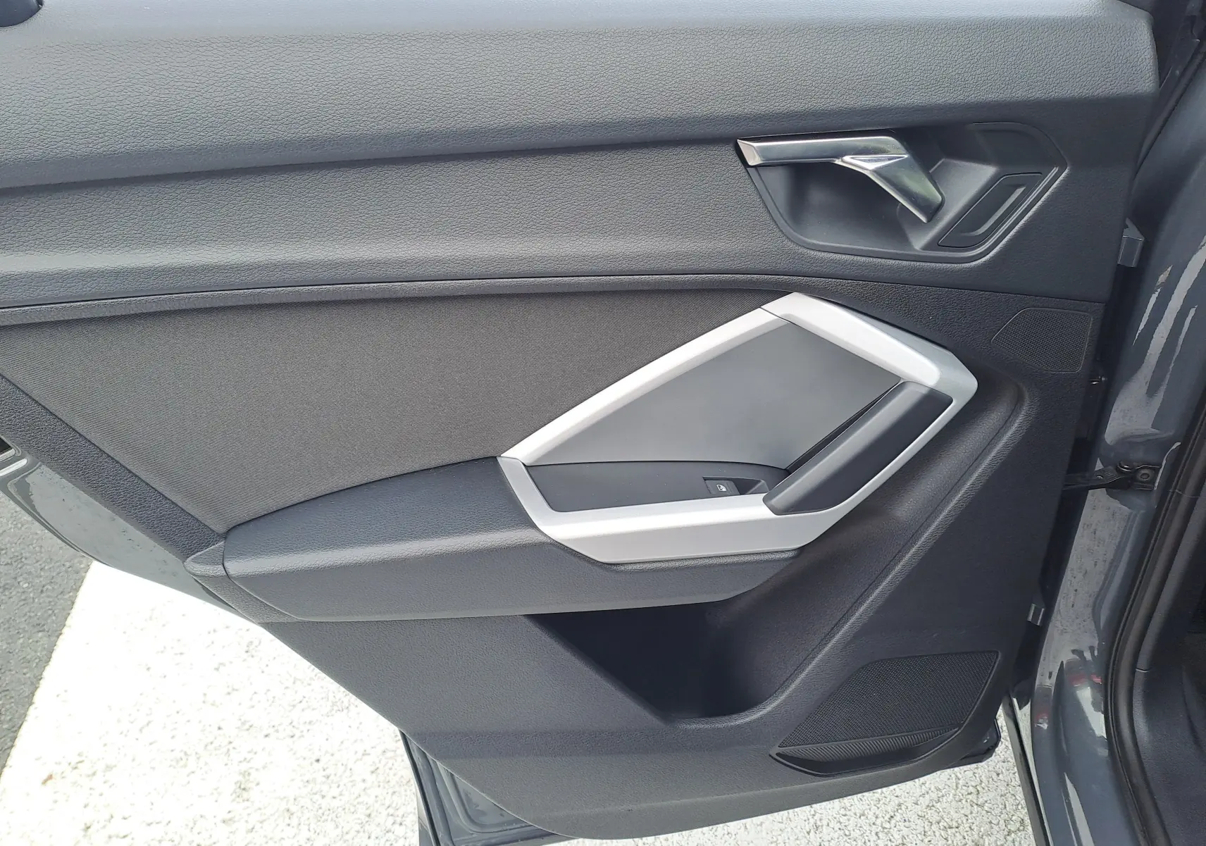 Détail de la porte avant gauche de l'Audi Q3 gris nano 2023, montrant la poignée et les commandes de fenêtre.