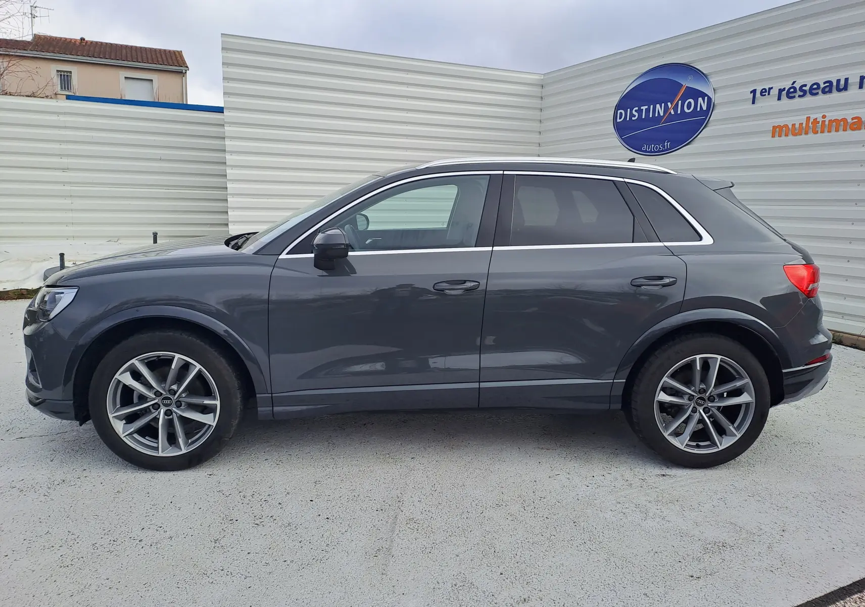 Profil droit d’un Audi Q3 35 TDI gris nano avec jantes alu 19 pouces, stationné devant un mur blanc.