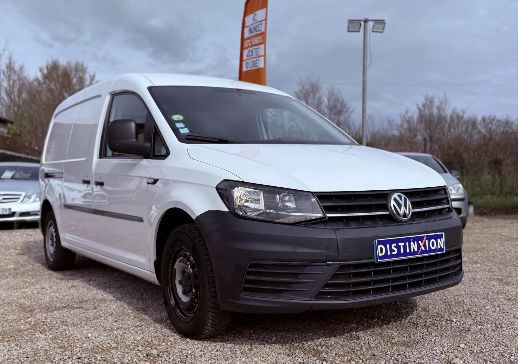 Vue 3/4 avant droit d’un utilitaire Volkswagen Caddy Maxi Long blanc avec pare-chocs noir mat sur un parking extérieur.