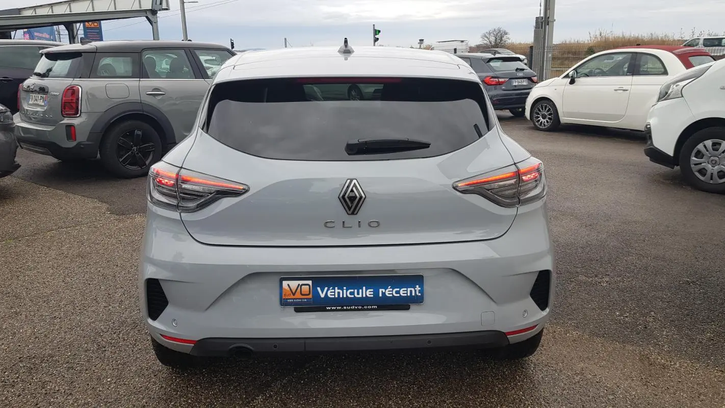 Vue arrière d'une Renault Clio gris clair 2025 avec feux LED allumés et vitres surteintées en stationnement.