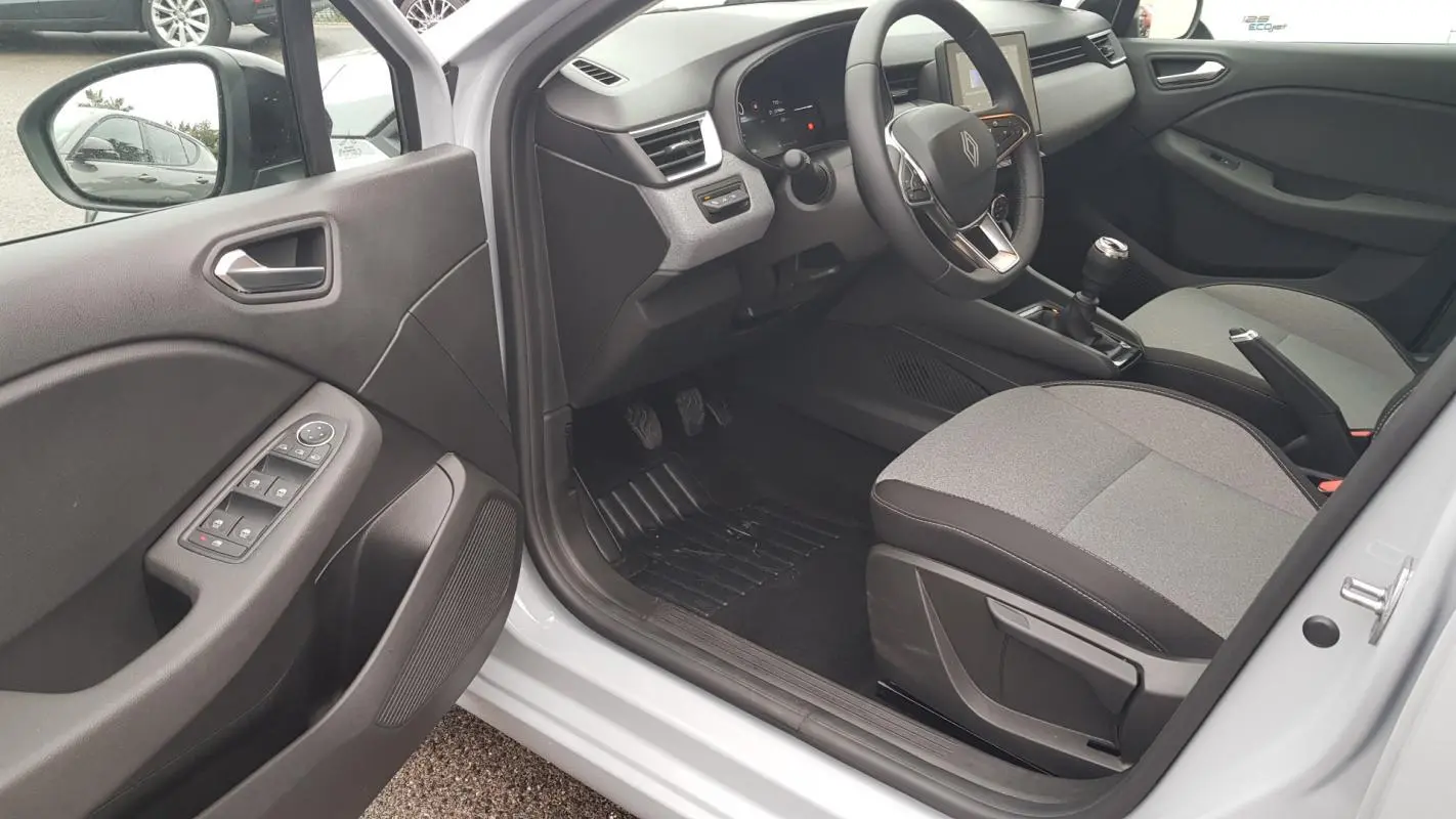 Vue intérieure côté conducteur de la Renault Clio gris 2025, montrant le tableau de bord et la boîte manuelle.